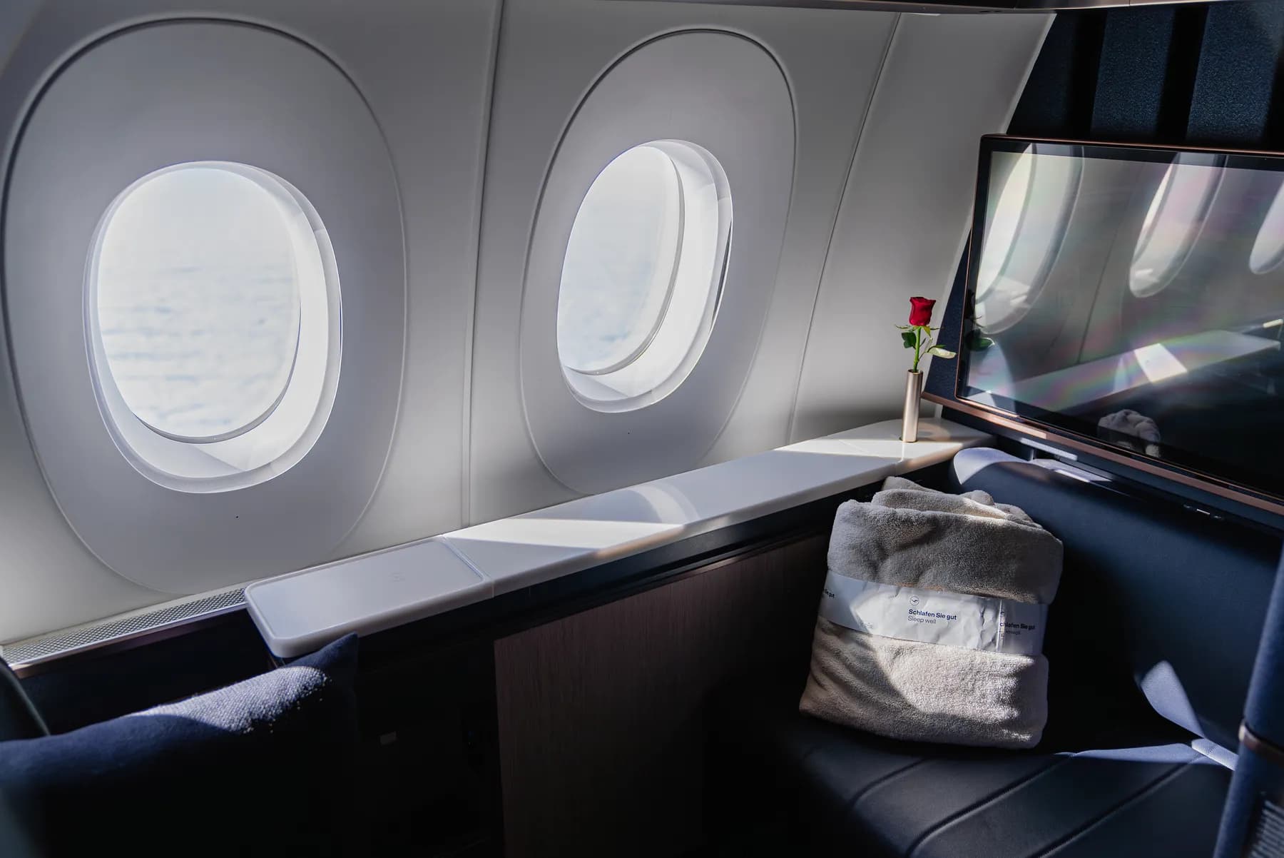 First-Class-Suite von Lufthansa Allegris mit großem Bildschirm, Fenstern und einer Rose auf der Ablage
