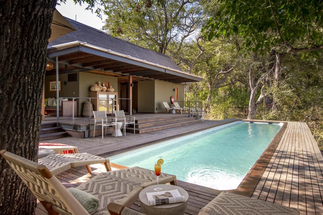 Pool und Deck der Chitabe Lodge im Schatten der Bäume